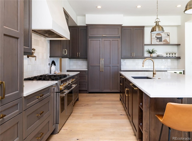 kitchen with double oven range, premium range hood, tasteful backsplash, a breakfast bar, and sink