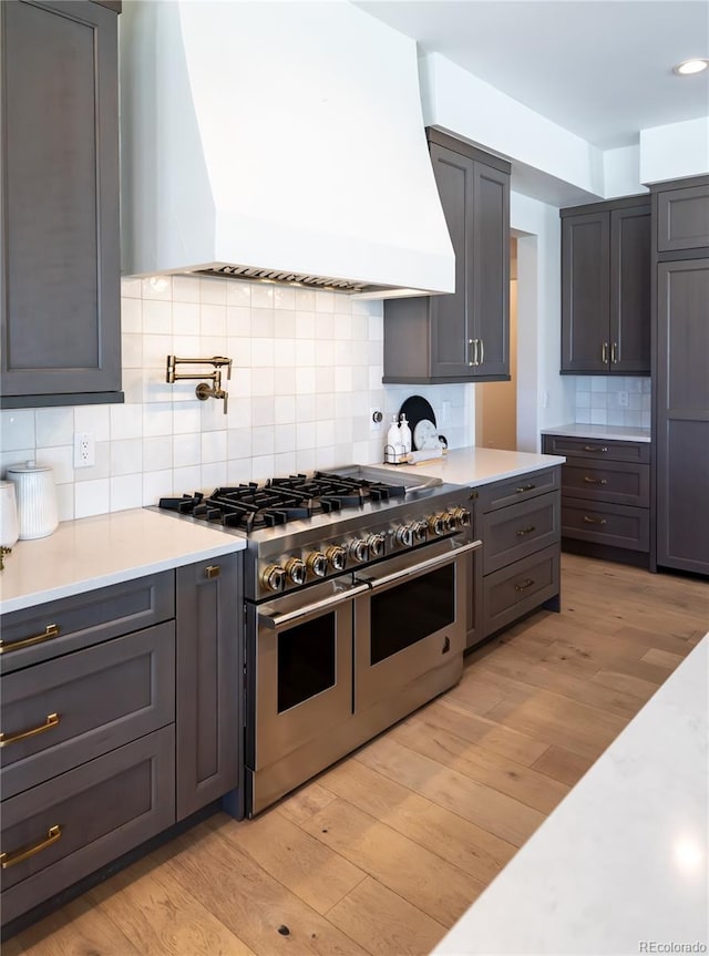 kitchen with custom exhaust hood, decorative backsplash, range with two ovens, and light hardwood / wood-style floors