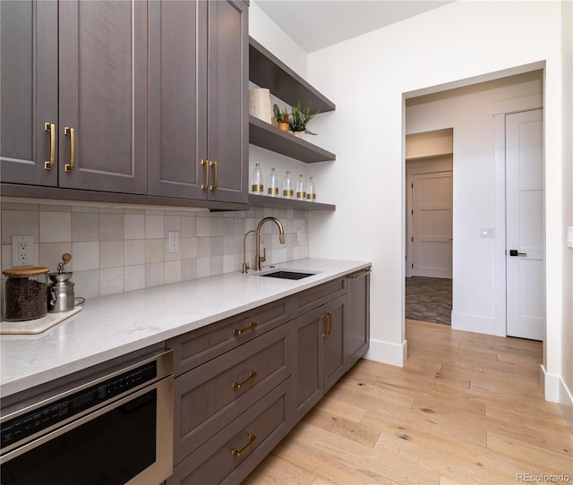 kitchen featuring backsplash, dishwasher, light hardwood / wood-style flooring, light stone counters, and sink