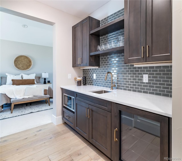 kitchen with wine cooler, stainless steel microwave, sink, dark brown cabinetry, and light wood-type flooring