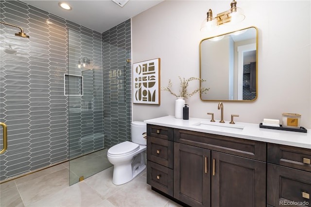 bathroom with toilet, tile patterned floors, tiled shower, and vanity