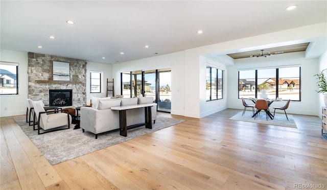 living room with a wealth of natural light, a stone fireplace, and light hardwood / wood-style flooring