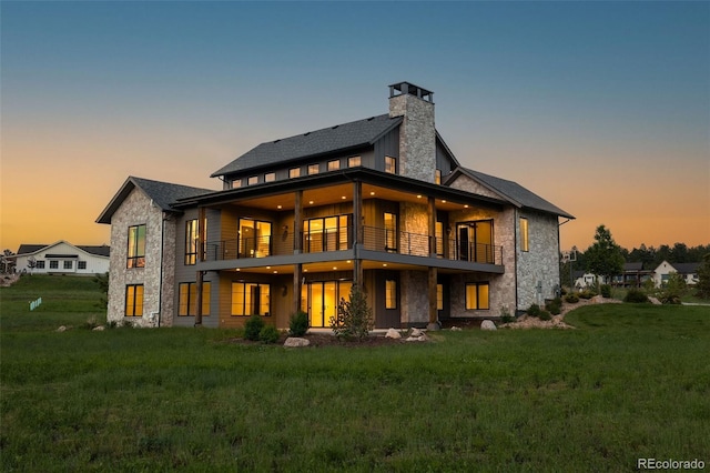 2442 Fox View Trl, Franktown, CO 80116 - back of house at dusk featuring a balcony, a yard, stone siding, and a chimney