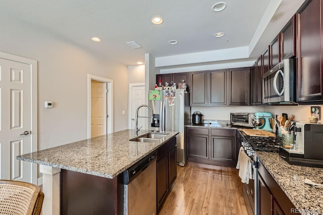 kitchen featuring light wood-type flooring, light stone counters, stainless steel appliances, sink, and a center island with sink