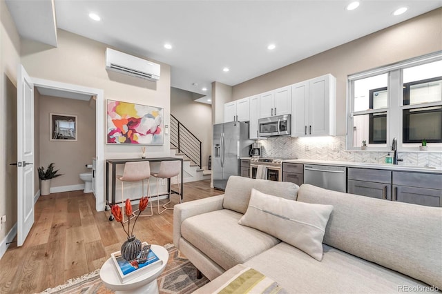 living room featuring stairs, a wall mounted AC, light wood-style flooring, and recessed lighting