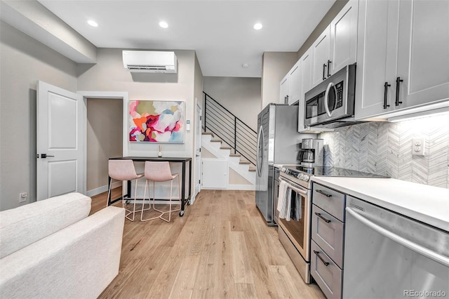 kitchen featuring light countertops, light wood-style flooring, decorative backsplash, appliances with stainless steel finishes, and an AC wall unit