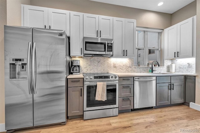 kitchen featuring light wood-style flooring, a sink, light countertops, appliances with stainless steel finishes, and backsplash