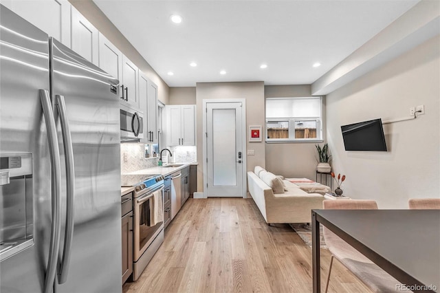 kitchen featuring stainless steel appliances, a sink, light wood-style floors, light countertops, and backsplash