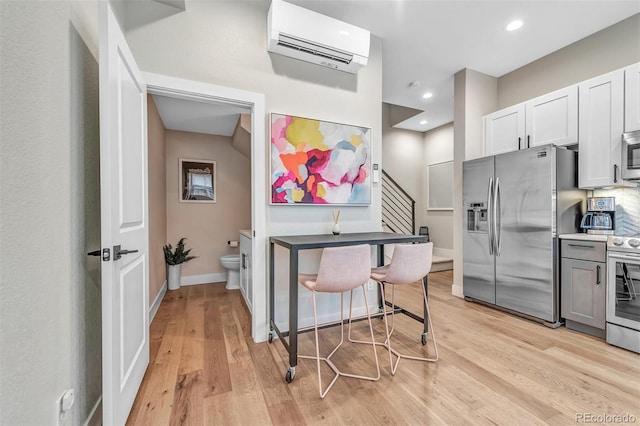 kitchen featuring light wood finished floors, baseboards, stainless steel appliances, an AC wall unit, and recessed lighting