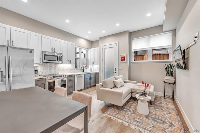 kitchen with baseboards, decorative backsplash, light wood-style flooring, stainless steel appliances, and a sink