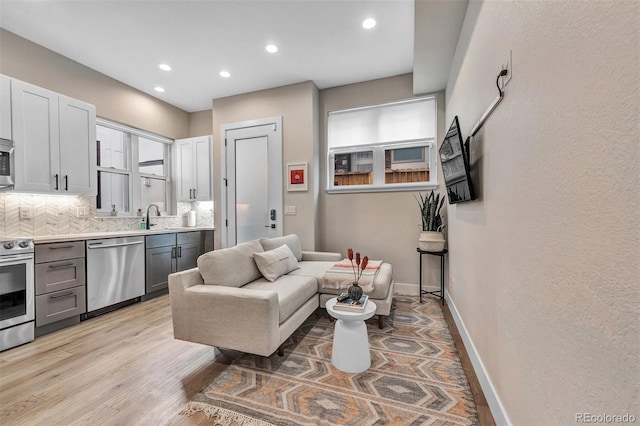 kitchen with stainless steel appliances, a sink, baseboards, light countertops, and decorative backsplash