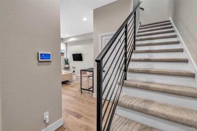 staircase with recessed lighting, baseboards, wood finished floors, and a textured wall