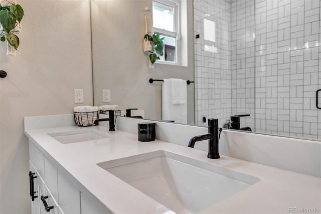 full bathroom with a tile shower, double vanity, and a sink