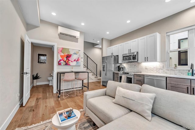 living room with baseboards, a wall unit AC, light wood-style flooring, stairs, and recessed lighting