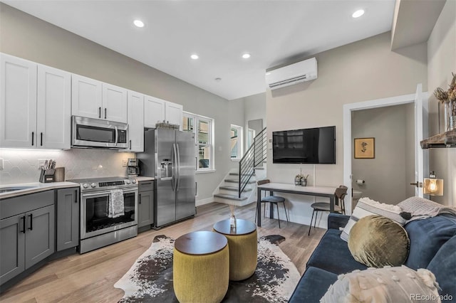 kitchen with light wood finished floors, decorative backsplash, open floor plan, a wall mounted air conditioner, and stainless steel appliances