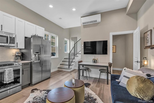 living room featuring an AC wall unit, baseboards, stairway, and light wood finished floors