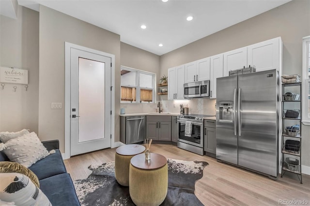 kitchen featuring stainless steel appliances, light wood-type flooring, a sink, and open shelves