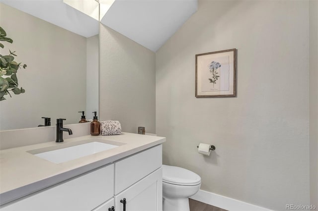 bathroom with toilet, wood finished floors, vanity, baseboards, and vaulted ceiling