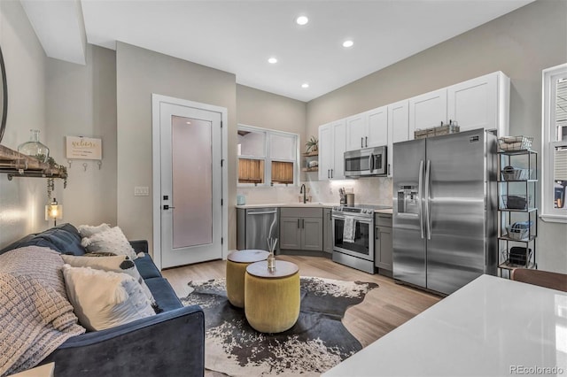 kitchen with open shelves, appliances with stainless steel finishes, a sink, and light wood-style floors