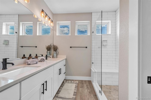 full bath featuring a tile shower, wood finished floors, a sink, and baseboards