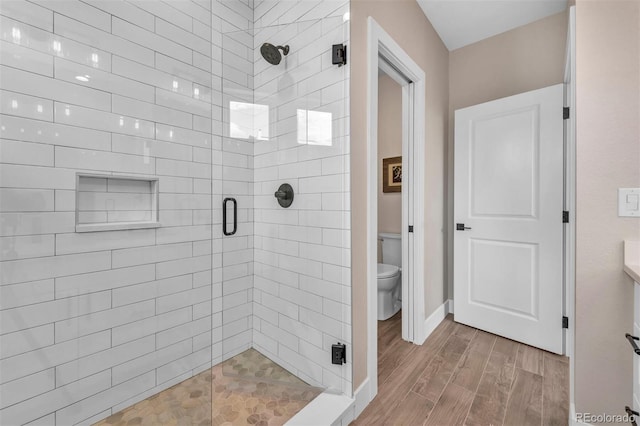 bathroom with toilet, a stall shower, baseboards, and wood finished floors