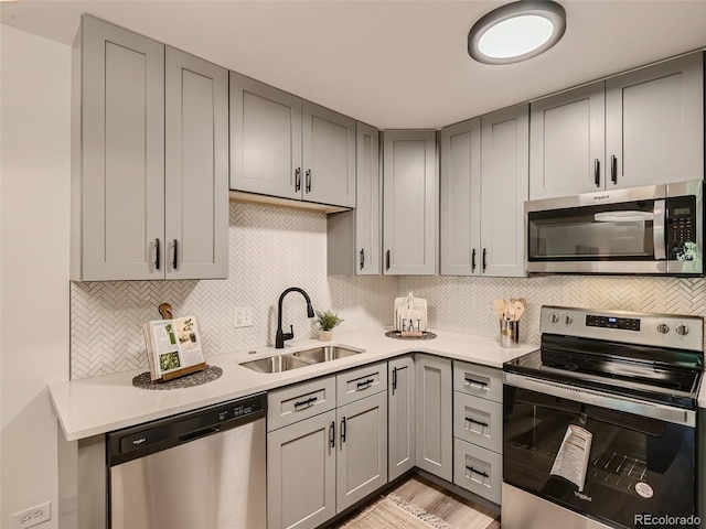 kitchen with light wood-type flooring, appliances with stainless steel finishes, gray cabinetry, and sink