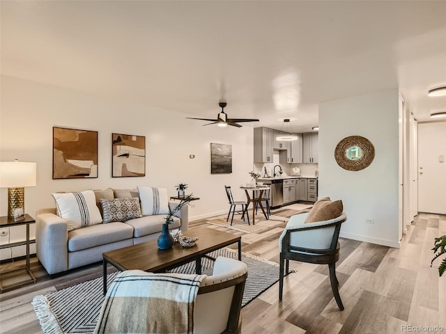 living room with light wood-type flooring, a baseboard heating unit, sink, and ceiling fan