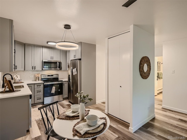 kitchen featuring gray cabinetry, pendant lighting, appliances with stainless steel finishes, decorative backsplash, and light wood-type flooring