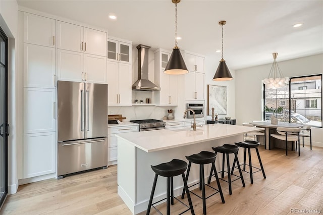3649 W 21st Ave, Denver, CO 80211 - kitchen featuring stainless steel appliances, wall chimney exhaust hood, light wood-type flooring, light countertops, and a center island with sink