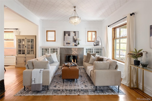living room featuring an inviting chandelier, ornamental molding, wood finished floors, and a high end fireplace