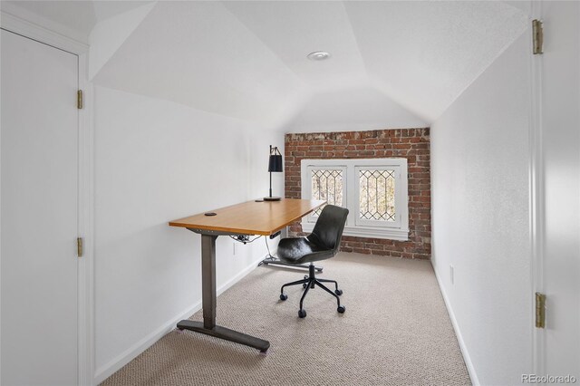 office space with baseboards, vaulted ceiling, carpet, and brick wall