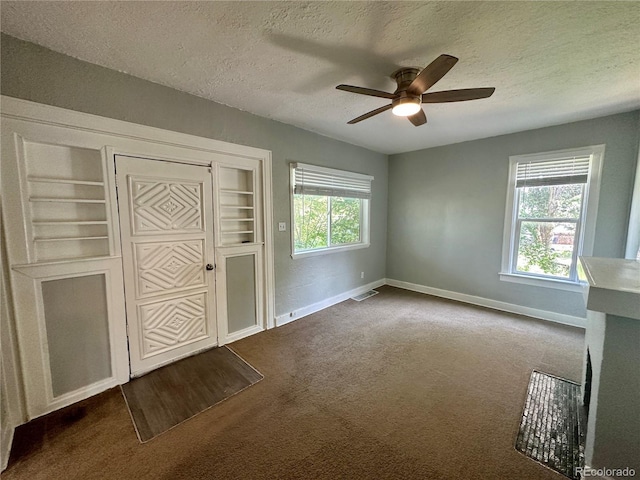 interior space featuring visible vents, a ceiling fan, a textured ceiling, dark carpet, and baseboards