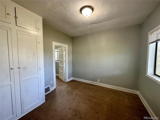 unfurnished bedroom featuring visible vents, baseboards, dark carpet, and a textured ceiling