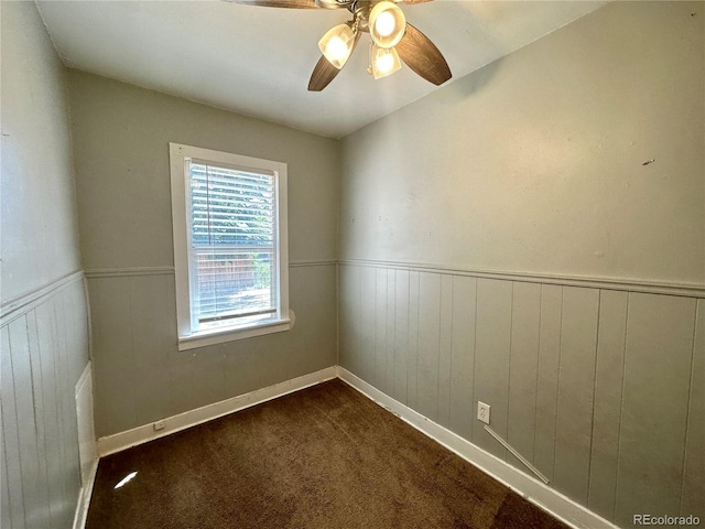 unfurnished room featuring a wainscoted wall, a ceiling fan, and dark colored carpet