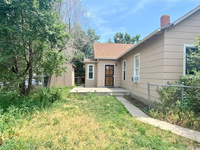 view of front of home featuring an outbuilding, fence, cooling unit, a storage shed, and roof with shingles