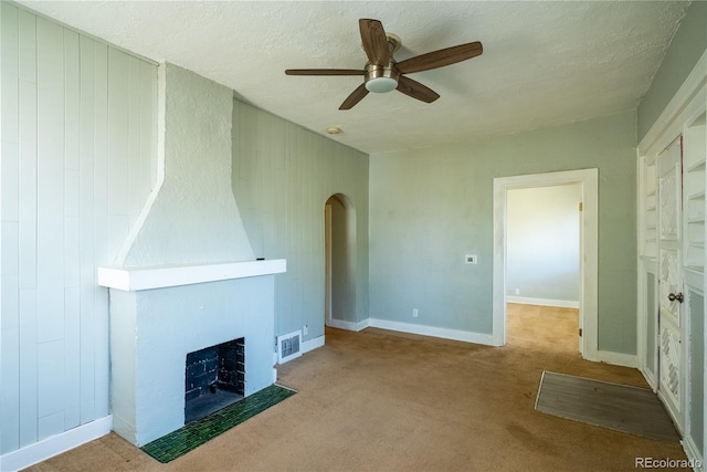 unfurnished living room with ceiling fan, carpet, arched walkways, a large fireplace, and visible vents
