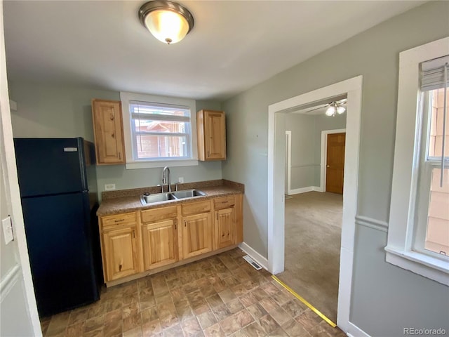 kitchen featuring visible vents, a sink, freestanding refrigerator, a ceiling fan, and light brown cabinetry