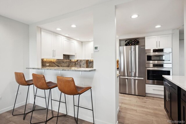 kitchen with stainless steel appliances, backsplash, light hardwood / wood-style floors, and white cabinetry