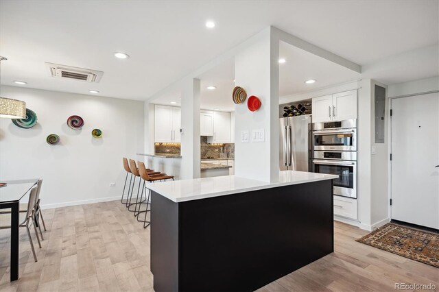 kitchen featuring white cabinets, backsplash, stainless steel appliances, and light wood-type flooring