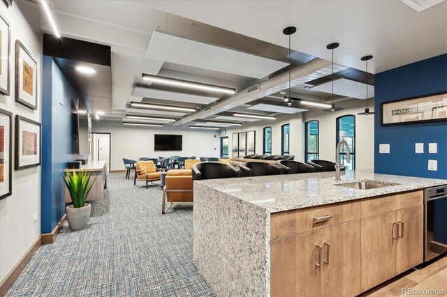 kitchen with hanging light fixtures, an island with sink, light stone countertops, stainless steel dishwasher, and sink