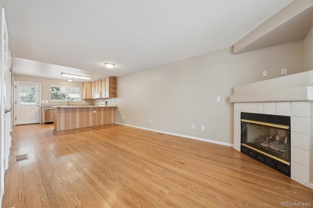 unfurnished living room featuring a textured ceiling, sink, a tile fireplace, and light hardwood / wood-style flooring