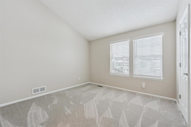 carpeted spare room with vaulted ceiling and a textured ceiling