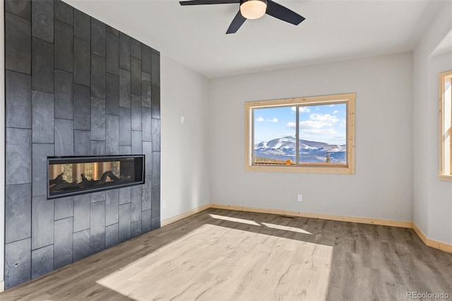 unfurnished living room featuring a multi sided fireplace, hardwood / wood-style floors, and ceiling fan