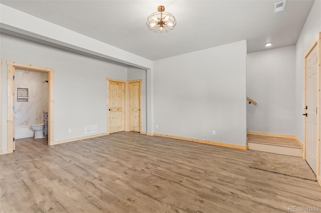 unfurnished bedroom featuring a notable chandelier, connected bathroom, and light wood-type flooring