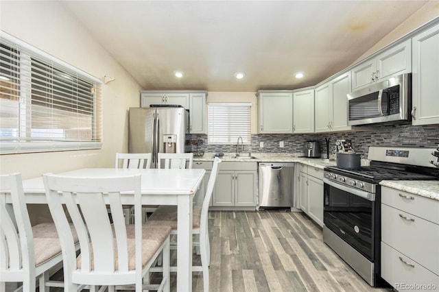 kitchen with sink, light stone counters, light hardwood / wood-style flooring, appliances with stainless steel finishes, and backsplash