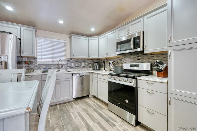 kitchen featuring appliances with stainless steel finishes, white cabinets, decorative backsplash, light stone countertops, and light wood-type flooring