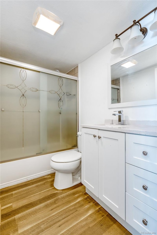 full bathroom featuring hardwood / wood-style flooring, bath / shower combo with glass door, vanity, and toilet