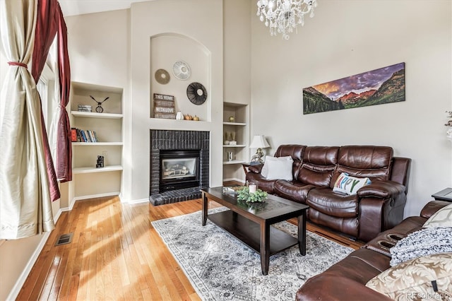 living room with a notable chandelier, a high ceiling, built in features, wood-type flooring, and a brick fireplace