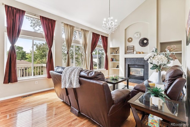 living room featuring an inviting chandelier, a fireplace, light hardwood / wood-style flooring, built in shelves, and high vaulted ceiling