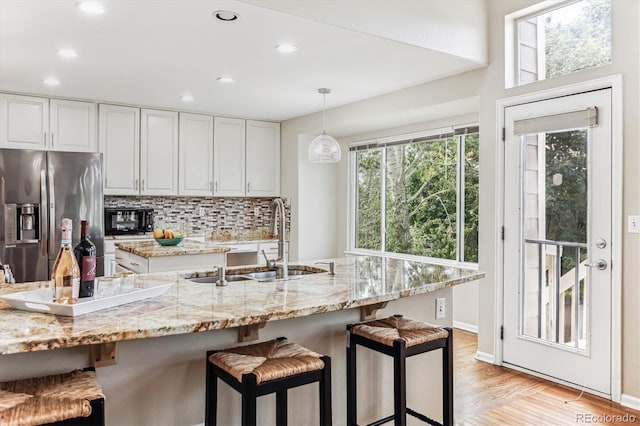 kitchen with stainless steel fridge with ice dispenser, white cabinetry, sink, and hanging light fixtures